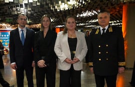 Un hombre en traje oscuro, una mujer en atuendo negro, otra con blusa blanca y un hombre en uniforme militar se encuentran de pie en un ambiente moderno.
