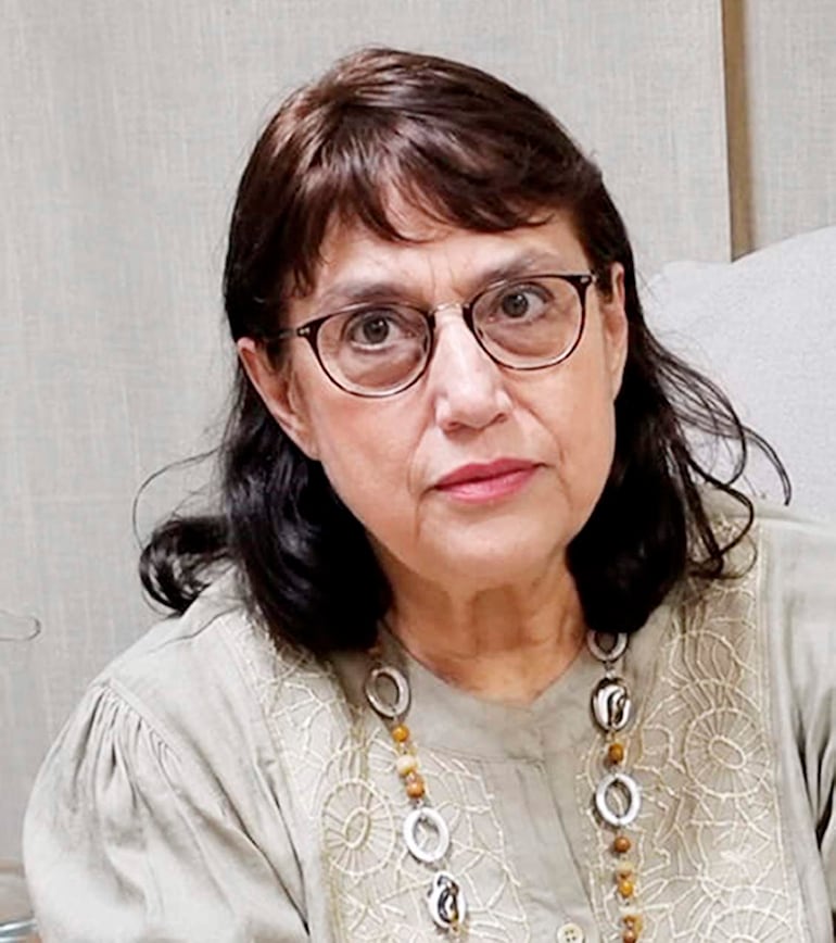 Ana Raquel Flores, con blusa clara y gafas, sentada en una oficina con fondo neutro.