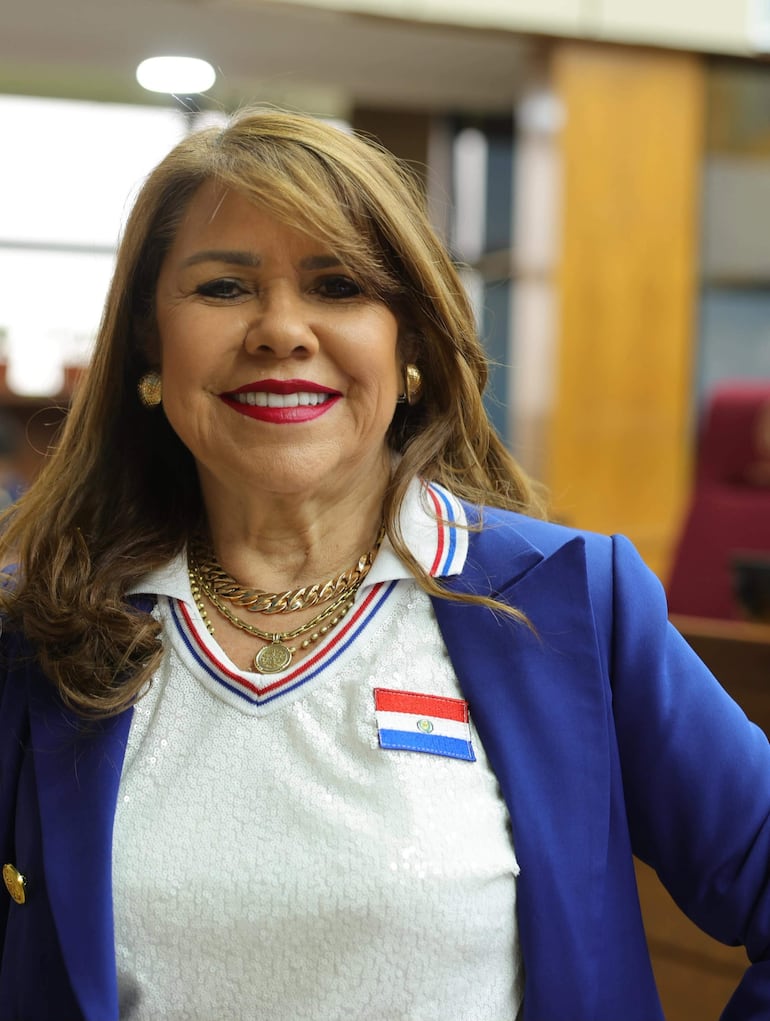 Celeste Amarilla sonriente con blusa blanca y saco azul, pin de la bandera paraguaya en la solapa, en un ambiente institucional.