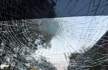 Cristal de vehículo roto por granizo, con patrón de fractura radial en un ambiente urbano con árboles y un semáforo.