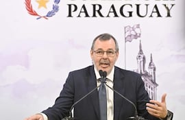 Carlos Carvallo en traje oscuro, en podio con micrófono, fondo con emblemas del Gobierno de Paraguay.