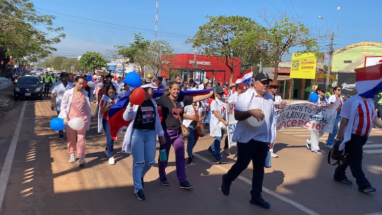 Médicos en camisetas blancas y detalles en rojo y azul, marchan con globos y un banner que dice 'Concepción'.