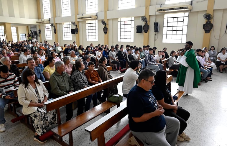 Sacerdote en ornamento verde habla a la congregación en la Iglesia San Vicente, con asistentes sentados en bancos de madera.