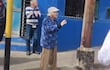 Mujer de cabello canoso en chaqueta azul bendice a médicos, con fondo urbano y expresión feliz.