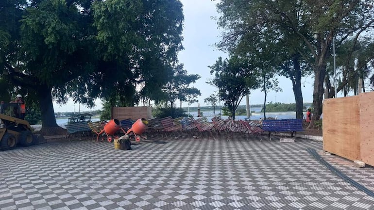 Obreros en la Plaza de los Desaparecidos, equipo de construcción en un área al aire libre rodeada de árboles y un lago.