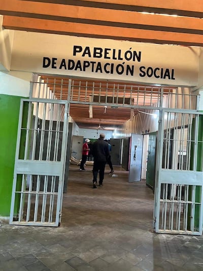 Hombres en el interior del Pabellón de Adaptación Social, uno con camiseta roja y otro con ropa oscura, en un ambiente colorido.