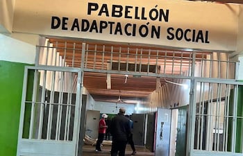 Hombres en el interior del Pabellón de Adaptación Social, uno con camiseta roja y otro con ropa oscura, en un ambiente colorido.