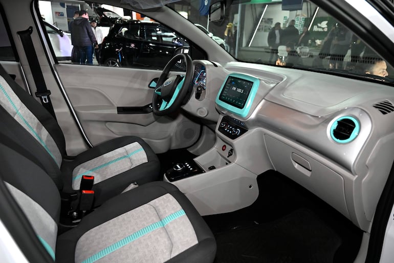 Interior de un vehículo con asientos gris y negro, detalles en azul, y tablero con pantalla digital mostrando FM 100.5.