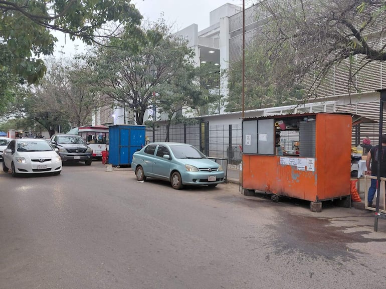 Vendedores en un puesto de comida frente al Hospital Ingavi, con vehículos estacionados y un entorno urbano moderno.