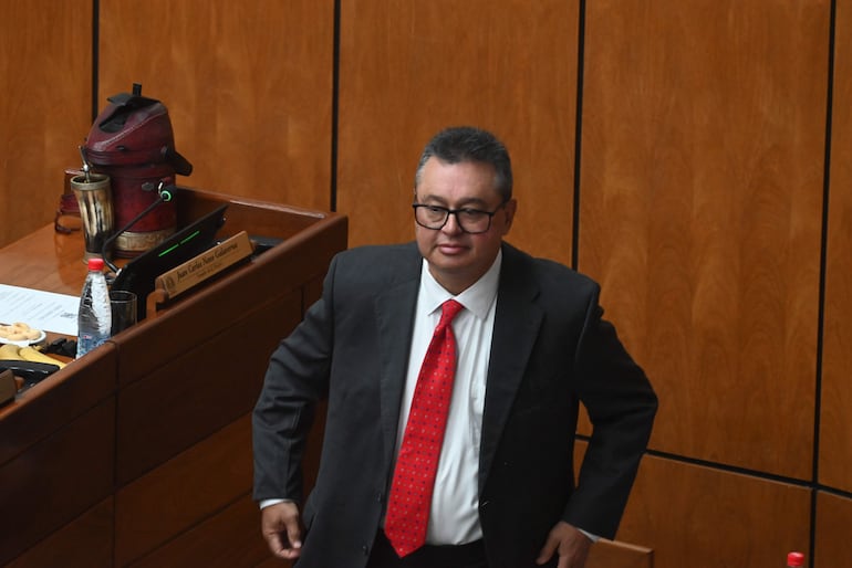 Gustavo Leite, con traje oscuro y corbata roja, se prepara para participar en una discusión en un recinto legislativo.