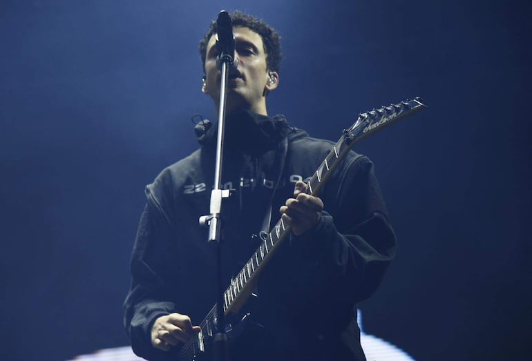 Jackson Jackson en chaqueta oscura, cantando con guitarra eléctrica y micrófono, en iluminación tenue en el escenario.