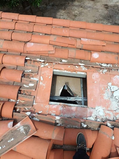 Techo de edificio con hueco y escombros, mientras una persona se inclina para observar el daño visible en la estructura.