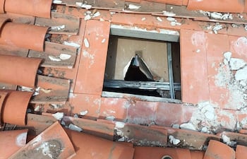 Techo de edificio con hueco y escombros, mientras una persona se inclina para observar el daño visible en la estructura.