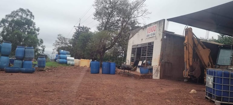 Establecimiento comercial muestra barriles azules apilados y letrero 'VENDO', en un ambiente rural.
