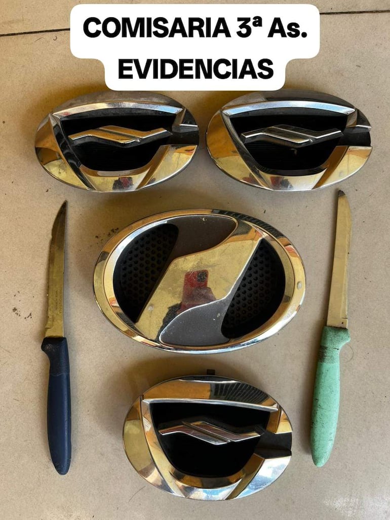 Objetos incautados en comisaría: emblemas Chevrolet y cuchillos sobre una superficie, sin personas visibles.