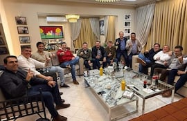 Hugo Meza, Marcelo Soto y otros hombres en un salón conversando alegremente, algunos levantan el dedo índice en un gesto festivo.