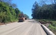 Rodillo compactador naranja avanza en la carretera en construcción bajo un cielo despejado en un entorno rural.