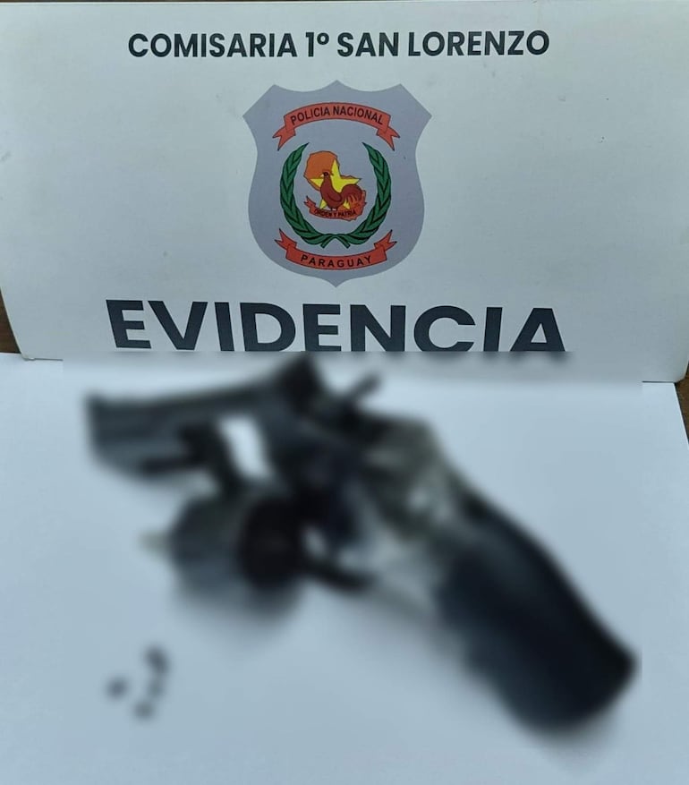 Arma de fuego sobre superficie blanca con cartel de Comisaría 1° San Lorenzo y la palabra 'EVIDENCIA' visible.