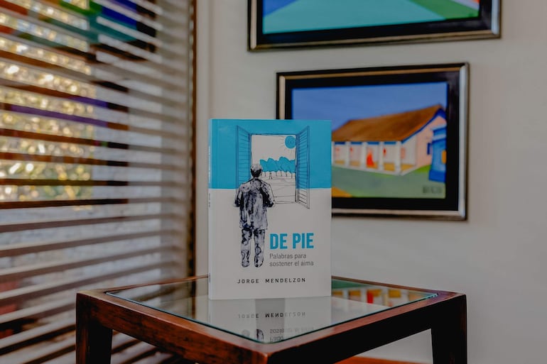 Libro 'De Pie' de Jorge Mendelzon sobre mesa de madera en ambiente acogedor con luz natural.