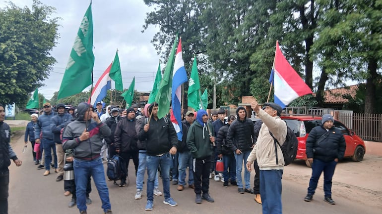 vdb Grupo de labriegos marchando, con banderas de Paraguay y verdes. Hombres abrigados escuchan atentamente al líder que sostiene la bandera.