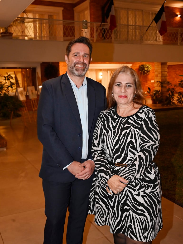 Hombre con traje oscuro y camisa blanca junto a mujer en vestido de cebra, ambos sonriendo en ambiente decorado con plantas.