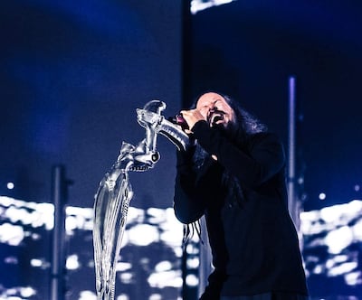 Hombre con cabello largo y oscuro, vestido de negro, canta con intensa concentración en un escenario iluminado.