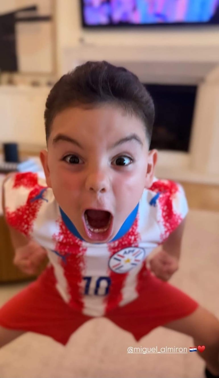 Niño enérgico con camiseta blanca y roja de la selección paraguaya, gritando con brazos levantados en un ambiente festivo.
