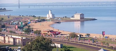 Panorámica costera en Encarnación, con un puente y un edificio singular. Ambiente tranquilo y recreativo, sin personas visibles.