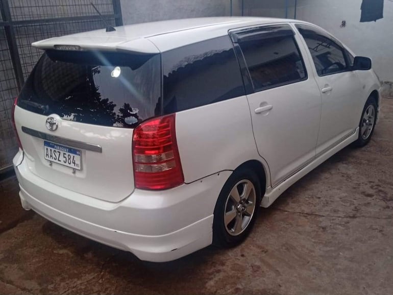 Vehículo Toyota blanco estacionado en garaje con paredes grises y malla que separa del exterior.