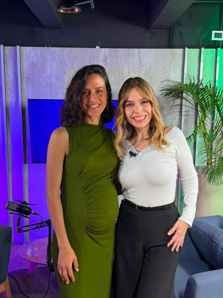 Fiorella Migliore y Belén Bogado sonríen de pie en un estudio, con vestimenta colorida y fondo decorativo de tonos claros y plantas.