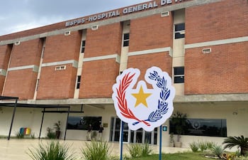Fachada de ladrillo del Hospital General de Itapúa, con vehículos estacionados y personas en la entrada en un día nublado.