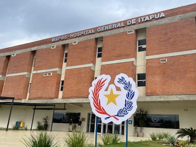 Fachada de ladrillo del Hospital General de Itapúa, con vehículos estacionados y personas en la entrada en un día nublado.