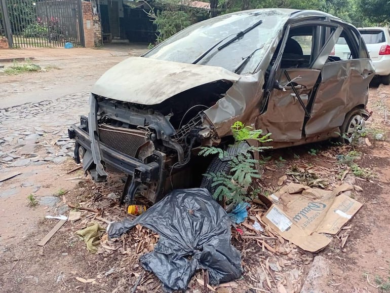 Automóvil gris dañado en la calle, con capó abierto y basura alrededor, reflejando abandono en el entorno urbano.