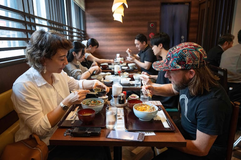 Esta fotografía, tomada el 8 de junio de 2026, muestra al turista estadounidense Wesley Smith (derecha) y a su esposa, Maya Bourdeau, almorzando en el restaurante Natto Kobo Sendai-ya, en Tokio.