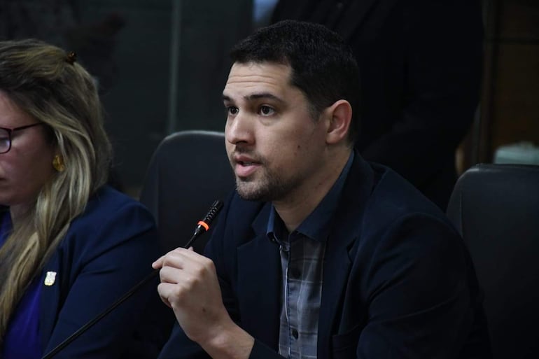 Pablo Callizo con expresión triste, en un ambiente formal con un hombre hablando detrás de un micrófono.