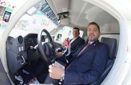 Pedro Alliana sonríe, sosteniendo llaves de ambulancia; el intendente lo observa, ambos en trajes formales dentro del vehículo.