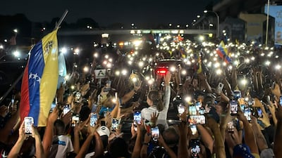 María Corina Machado saluda a seguidores en un ambiente festivo nocturno con teléfonos móviles encendidos y banderas de Venezuela.