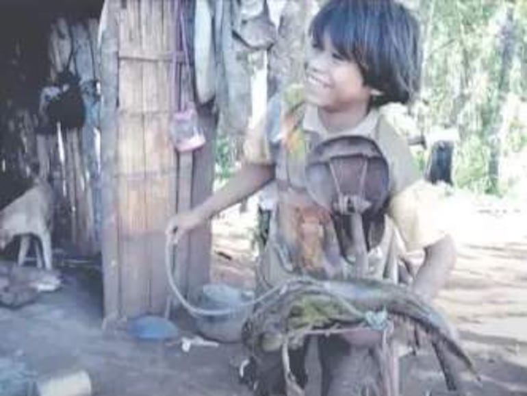 Niño de cabello oscuro y desgastado sonríe mientras sostiene un artilugio de madera, acompañado de un perro en un ambiente rural.