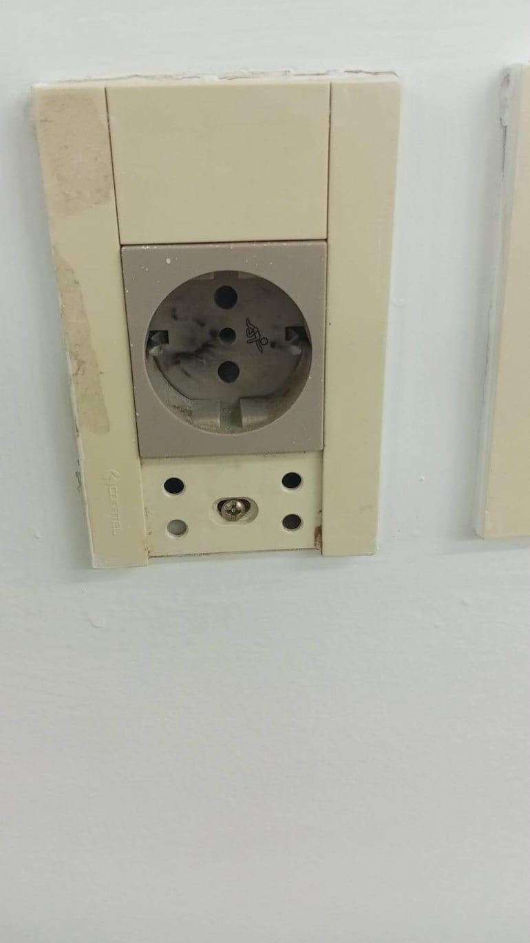 Tomacorriente beige en pared blanca con marcas visibles de uso, sin personas presentes.