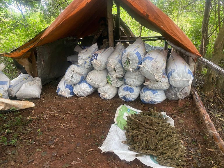 Estructura improvisada cubierta por lona naranja y sacos apilados en un área rural, sin personas visibles.