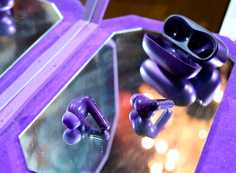 Auriculares inalámbricos púrpuras sobre superficie reflectante, destacando un diseño moderno y caja de carga.