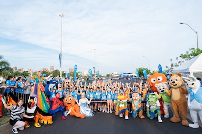 Multitud de personas sonrientes levantan las manos, vistiendo camisetas azules en un ambiente festivo con decoraciones.