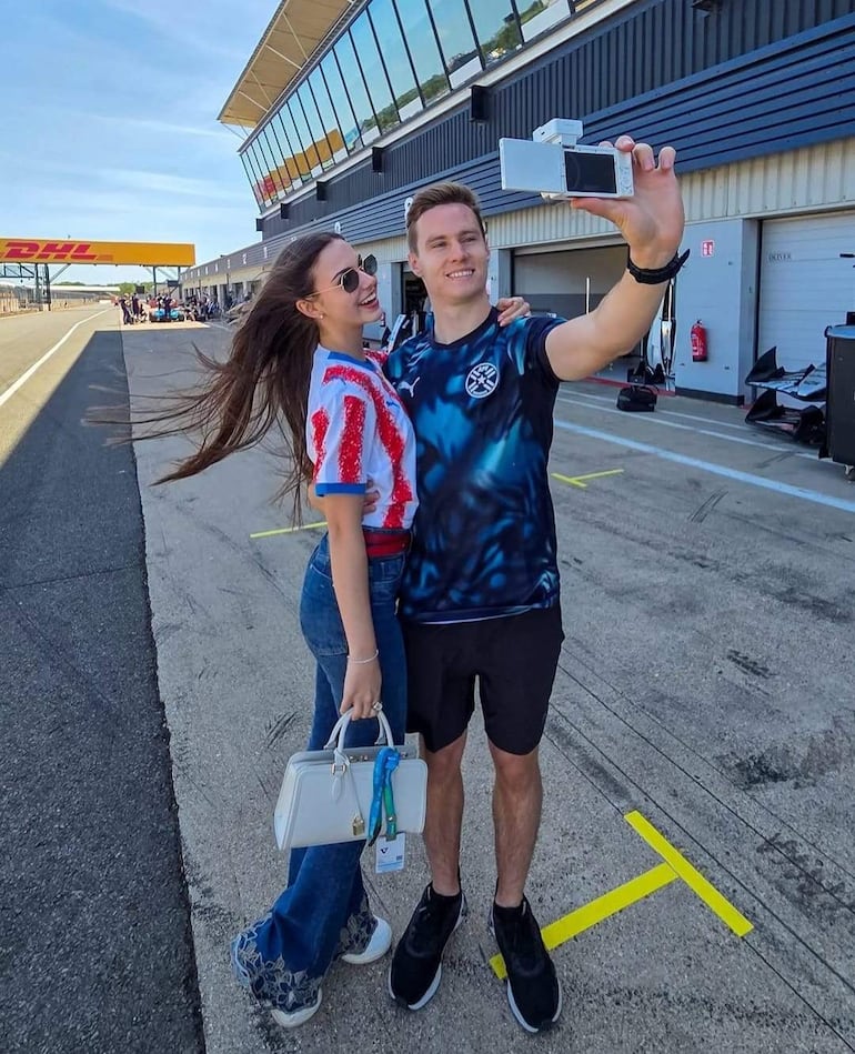 Joshua Duerksen sonríe sosteniendo una cámara, mientras Anneke Rahn viste camiseta de la bandera paraguaya y sonríe cerca de él.