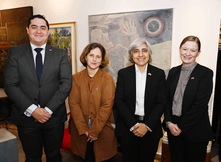 Linda Taiyen, vestida con chaqueta marrón, sonríe junto a tres personas en un entorno artístico, todos con trajes formales.