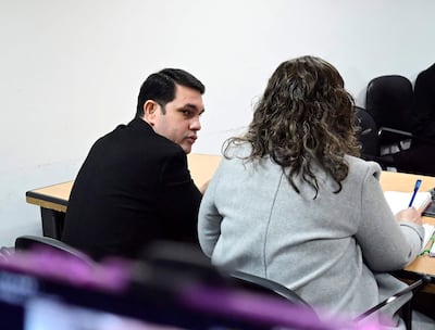 Rivas, vestido con suéter negro, escucha atentamente mientras su defensora, con abrigo gris y cabello rizado, escribe en un cuaderno.