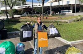 Soledad Núñez, con camisa de mezclilla y jeans, sostiene bolsas de basura frente a la Municipalidad de Asunción, rodeada de hombres de seguridad.