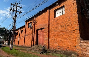 Vista del antiguo Teatro El Molino, edificio de ladrillos rojos con puerta de madera y poste eléctrico cercano.