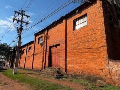 Vista del antiguo Teatro El Molino, edificio de ladrillos rojos con puerta de madera y poste eléctrico cercano.