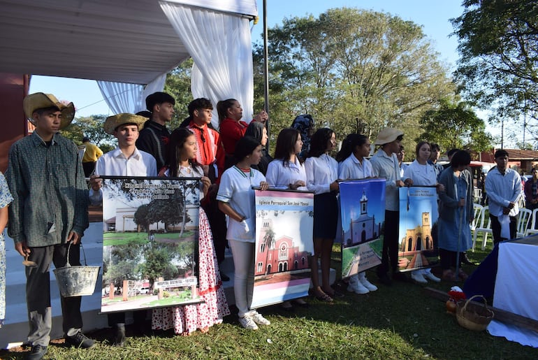 Grupo de jóvenes con vestimenta tradicional sostiene carteles sobre iglesias de Ybycuí, en un ambiente diurno y festivo al aire libre.