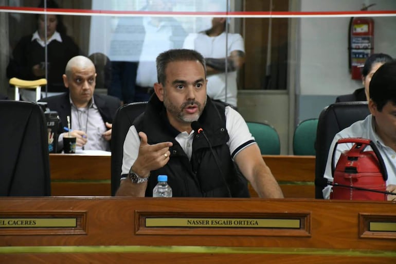 Hombre con chaleco gesticulando durante reunión, mientras otros escuchan y toman notas en ambiente institucional.
